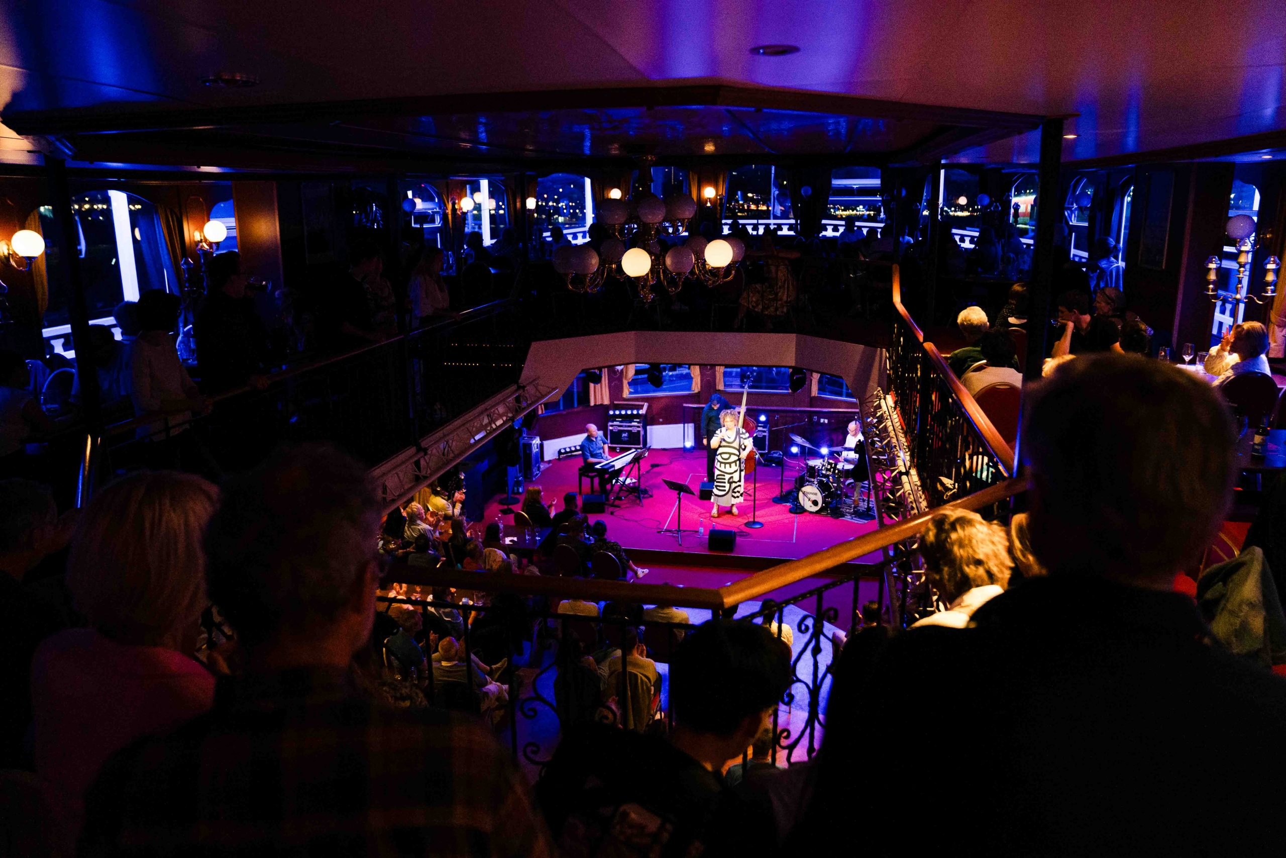 Blick von der Galerie auf die Winter Jazz Cruise in Hamburg: Bühne mit Sängerin und Band auf der MS Louisiana Star, stimmungsvolle Beleuchtung und begeistertes Publikum genießen den Live-Jazz.