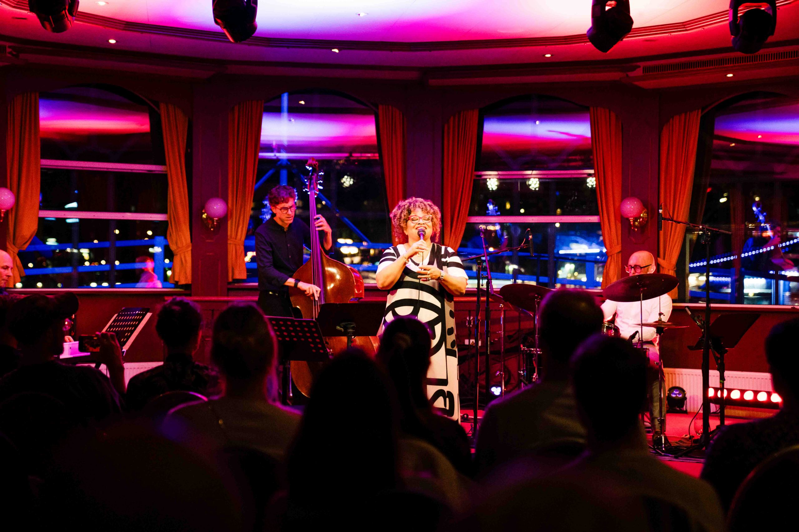 Live-Jazz auf der Winter Jazz Cruise in Hamburg: Sängerin performt mit Kontrabassist und Schlagzeuger auf der MS Louisiana Star, festlich beleuchtete Bühne und begeistertes Publikum.